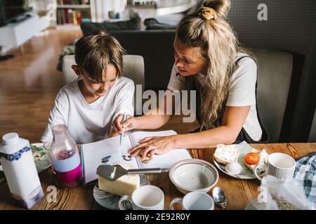 Mother teaching son while having breakfast in living room Stock Photo