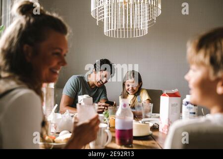 Happy father and daughter using smart phone at dining table Stock Photo