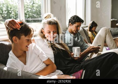 Smiling son with digital tablet sitting by mother in living room Stock Photo