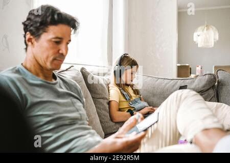 Father using smart phone while daughter e-learning through laptop in living room Stock Photo