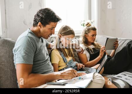 Father teaching daughter while mother sitting beside using digital tablet at home Stock Photo