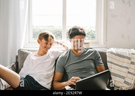 Happy father using laptop while sitting by son in living room Stock Photo