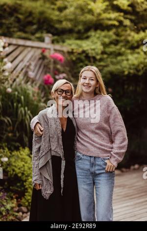 Smiling granddaughter with arm around of grandmother in back yard Stock Photo