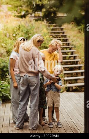 Elder sister showing smart phone to siblings while standing in back yard Stock Photo