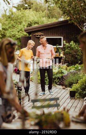 Father and son walking with bowl and plate in back yard during social event Stock Photo
