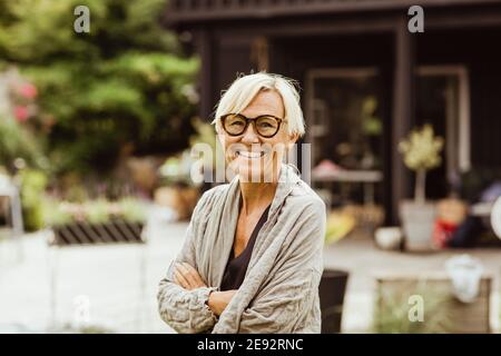 Smiling mature woman with arms crossed in back yard Stock Photo