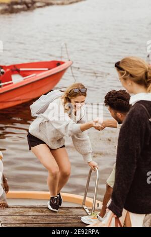 Man helping smiling female friend to climb on jetty Stock Photo