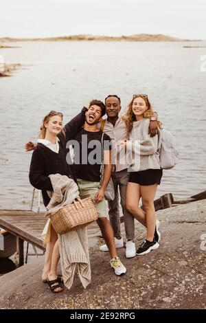 Portrait of smiling friends standing against sea during summer vacation Stock Photo