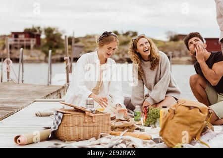 Friends laughing while having snacks during picnic at harbor Stock Photo
