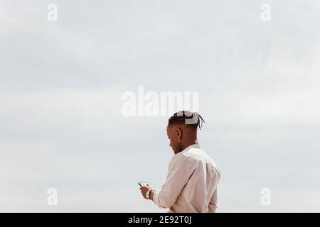 Young man using smart phone against clear sky on sunny day Stock Photo