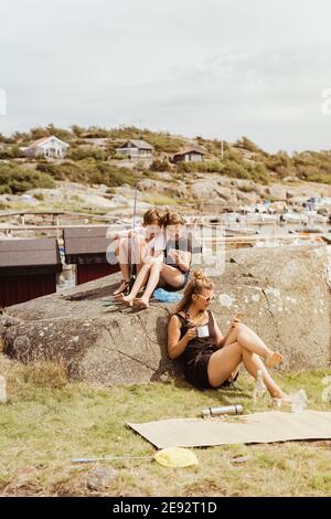 Siblings and mother using mobile phone while sitting at marina Stock Photo