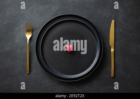 Candy heart on black plates with golden cutlery on black table. Top view on Valentine's day table setting. Stock Photo