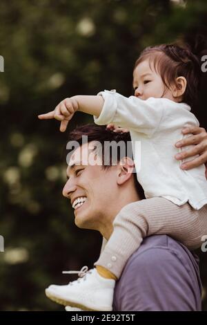 Male toddler pointing while sitting on father's shoulder at playground Stock Photo