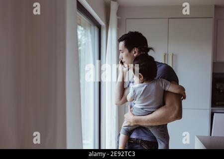 Father talking on mobile phone while carrying son at home Stock Photo