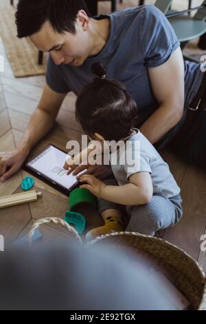 Father using digital tablet sitting with baby son at home Stock Photo