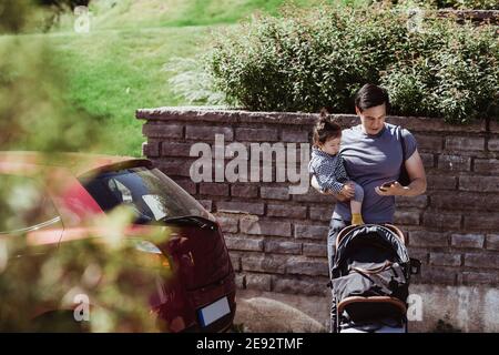 Father using smart phone while carrying baby son on sunny day Stock Photo