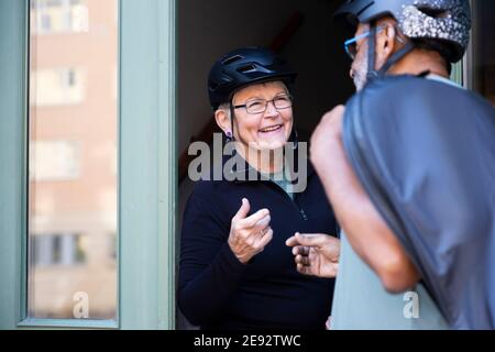 Smiling senior couple with cycling helmet on doorway at home Stock Photo