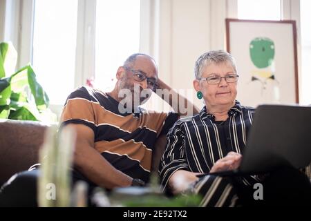 Woman using laptop while man sitting by on sofa Stock Photo