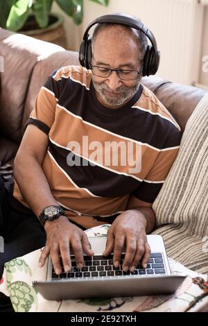 Elderly man listening music on headphones while using laptop in living room Stock Photo