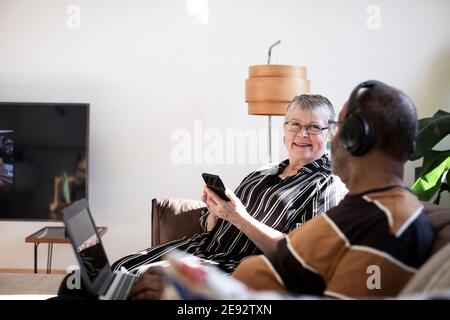 Senior couple with smart and laptop sitting on sofa in living room Stock Photo