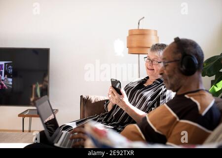 Woman using smart phone sitting by man with laptop at home Stock Photo