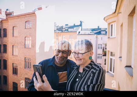Senior couple taking selfie through mobile phone in balcony Stock Photo
