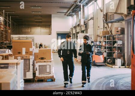 Female and male colleagues discussing over digital tablet while walking in warehouse Stock Photo