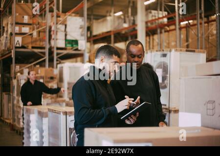 Male manual workers discussing over digital tablet at warehouse Stock Photo