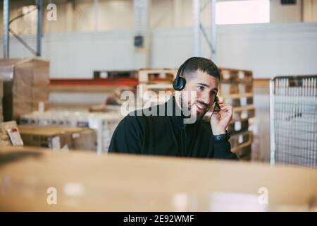 Male manual worker talking through headset at logistics warehouse Stock Photo