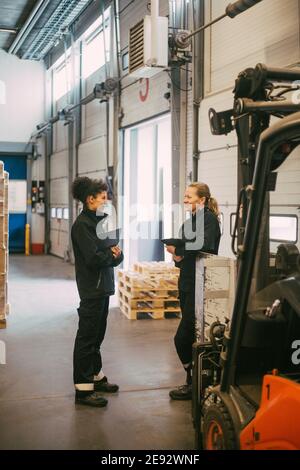 Female manual workers discussing while standing in distribution warehouse Stock Photo