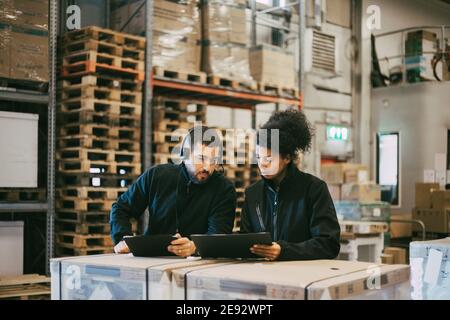 Male and female colleagues discussing while using digital tablet at logistics warehouse Stock Photo
