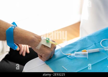 High angle of crop unrecognizable doctor with needle taking blood sample from senior female patient