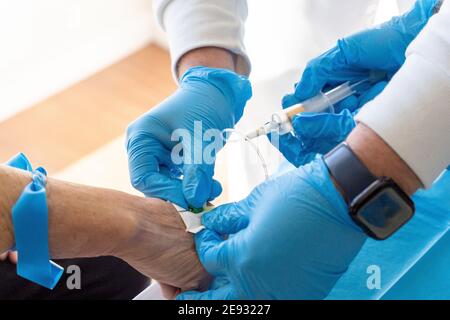 From above of crop anonymous doctors with needle and syringe taking blood sample from elderly female patient