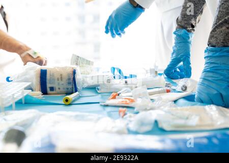 Crop anonymous doctors in protective gloves and patient at table with assorted medical tools for COVID 19 diagnostic Stock Photo