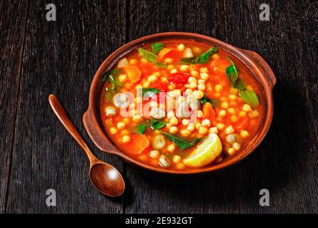chickpea and green broad bean Moroccan soup in an earthenware bowl on a rustic wooden table, close-up Stock Photo