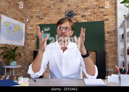 Caucasian male teacher giving online lesson sitting at desk explaining Stock Photo