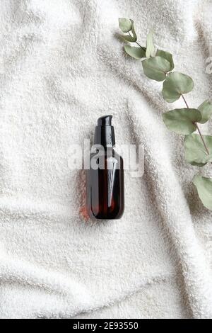 Natural herbal cosmetic. Amber glass bottle with serum and eucalyptus leaf on white towel in bathroom. SPA organic beauty product. Top view, flat lay. Stock Photo
