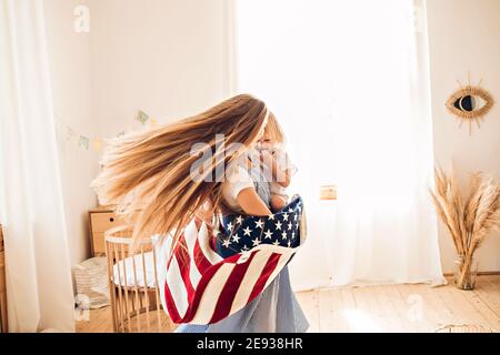Young mother or babysitter with a little girl in her arms spin in the middle of the room celebrating July 4th Independence Day Stock Photo