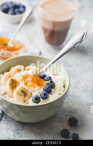 Breakfast with Milk rice porridge with banans, blueberry and orange jam, creamy rice pudding or french riz au lait in a bowl, glass cup with cocoa and Stock Photo