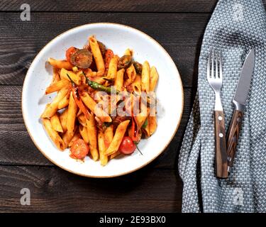 Rigatoni arrabiata with fiery tomato sauce on a brown wooden table with a fork and a knife Stock Photo