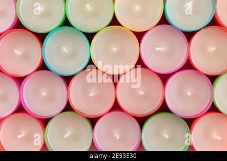 Top view of rows of unused multicolored wax tea light candles. Row of new water candles as background. A lot of candles on pink background, close-up. Stock Photo
