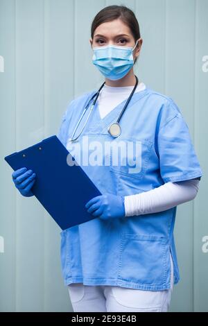 EMS UK paramedic woman wearing personal protective equipment PPE holding clipboard,standing in front of ICU facility hospital,novel Coronavirus pandem Stock Photo
