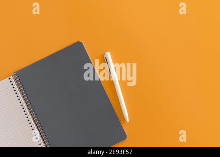 Spiral opened notebook with gray sheet and white pen. Layout and flat lay with place for text  on orange background. Back to school. Top view, copy sp Stock Photo
