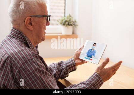 Retired senior elderly man talking to NHS GP female doctor via virtual telemedicine video call using tablet,online medical professional consultation Stock Photo