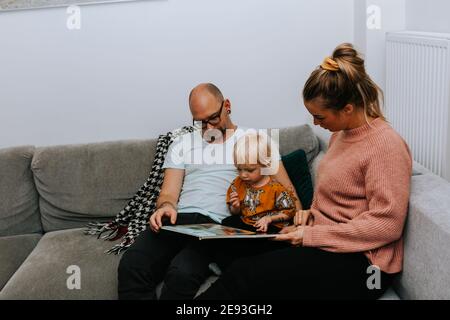 Parents reading toddler book on sofa Stock Photo