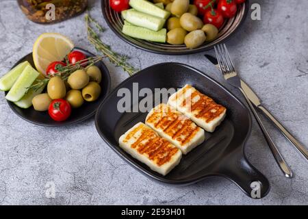 Grilled haloumi cheese on a black pan with olives, tomatoes, cucumbers and pepperoni. Close-up.