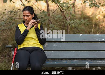 Visually impaired woman sitting on bench and using cell phone Stock Photo