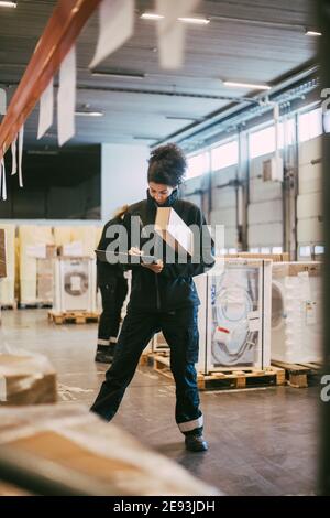Businesswoman writing on clipboard while analyzing packages at warehouse Stock Photo