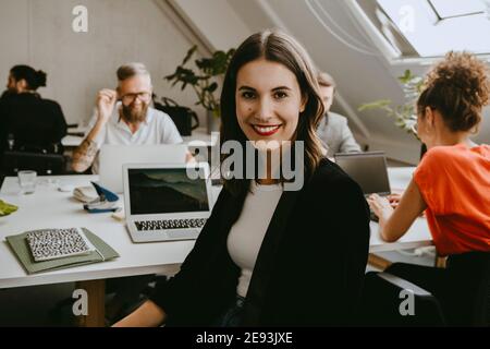 Smiling young businesswoman sitting with colleagues in coworking office Stock Photo