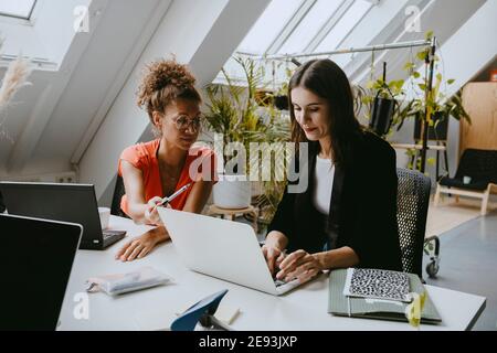 Female colleagues discussing over laptop at coworking office Stock Photo